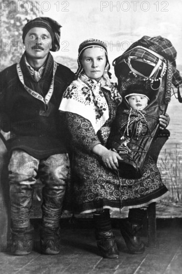 Sami in traditional dress with baby, 1930s, A traditionally dressed couple with a baby swaddled in traditional traditional costume sit for a family portrait, Historical photograph