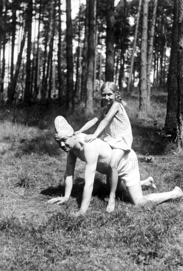 Girl riding on her father's back, 1930s, A girl rides happily on a man kneeling on all fours in the sunny forest, Historical photo