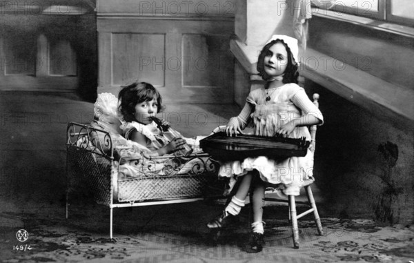 Two children making music, 1920s, Two girls, one in bed and one on a chair, playing in an old interior, Historical photo