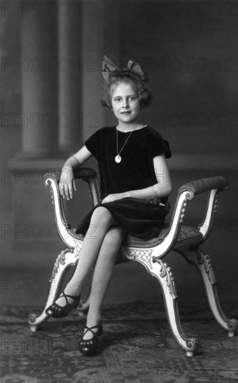 Distinguished girl, 1920, A girl sits solemnly on an ornately decorated chair, wearing a pearl necklace, Historical photo