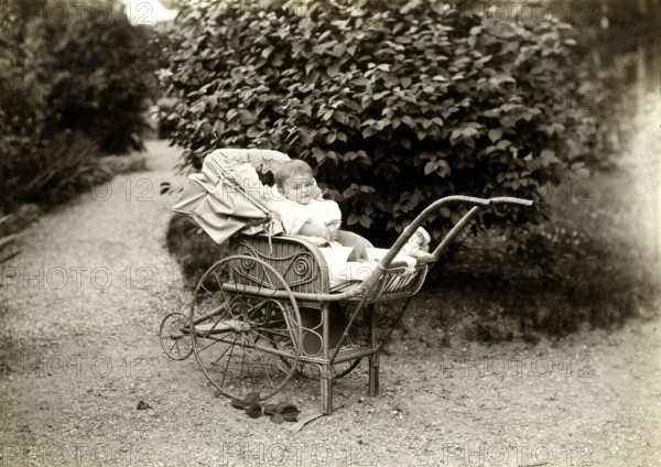 Baby in a pram, 1920, A toddler sits smiling in an antique pram in a garden, Historical photo