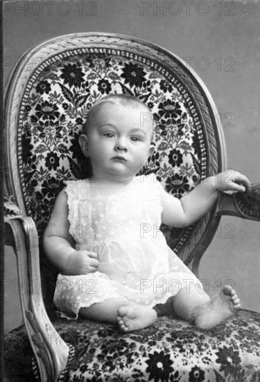 Baby sitting in armchair, 1911, A baby in a pretty, patterned armchair, looking attentively, Historical photo