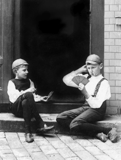 Two children playing cards, 1930s, Two boys in period clothing playing cards on a staircase, Historical photo