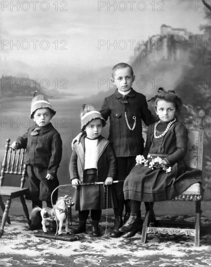 4 siblings, 1900, Four formally dressed children posing with toys and chairs, Historical photo