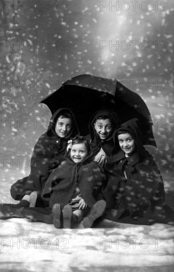 4 children in the snow, 1930s, A family sits under an umbrella in the snow for a group portrait, Historical photo