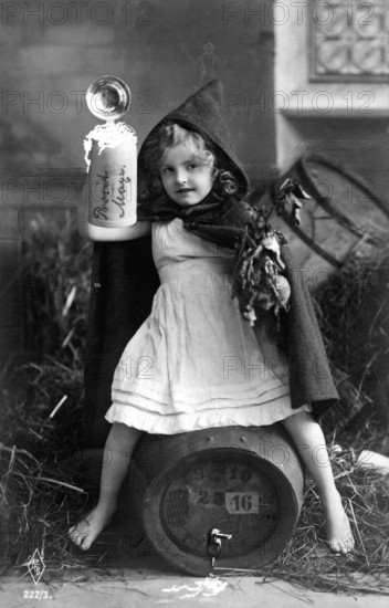 Girl drinking beer, ca. 1920, A girl with a hood is sitting on a barrel, holding an object in a fairytale scene, Historical photo