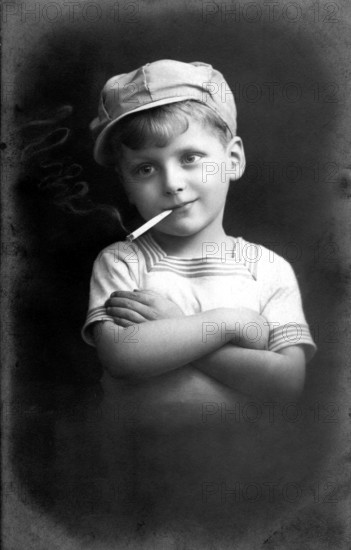 Boy smoking, 1920, Black and white photo of a boy with cap and cigarette in a casual pose, historical photo