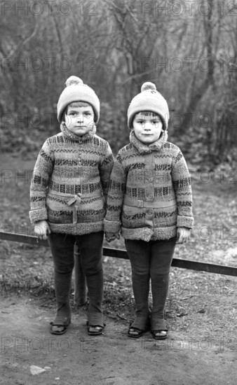 2 boys, twins, 1920, Two identical children in winter clothes standing next to each other outdoors, Historical photo
