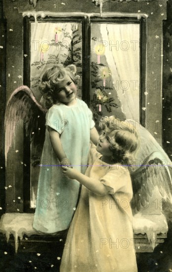 2 children as angels, 1920, Two children dressed as angels dancing in front of a decorated window, Historical photo