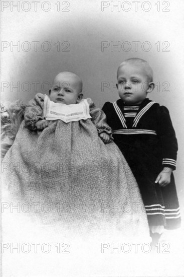 2 siblings, 1900, Two small children in a photo studio, one in a long dress, Historical photo