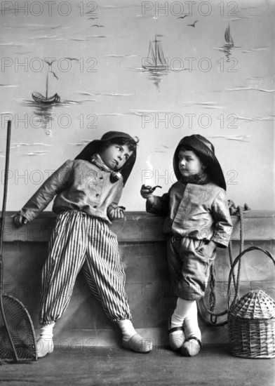2 Dutch boys with pipe, 1920, Two boys in fantasy costumes, a little bit turned on, with sailing ship background, historical photo