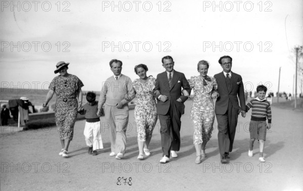 Family outing on the beach promenade, 1930s, A group of people stroll along the beach in elegant clothing, Historical photo