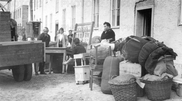 Refugees from the GDR loading lorries with furniture, 1960s, people standing next to furniture and boxes in a moving scenario in front of a building, historical photo