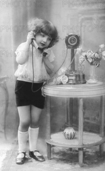 Child on the telephone, 1920s, A girl speaks into an old telephone, flowers on the table, Historical photo