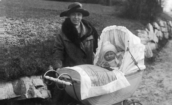 Woman with pram, 1910s, Woman with hat and coat standing with a baby in a pram on a country road, historical photo