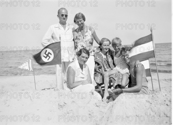 National Socialist family on holiday, Baltic Sea, Beach, 1930s, A family poses on the beach, next to them is a flag with a swastika, Historical photo