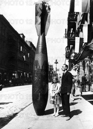 Father and child next to bombs, 1940s, A man and a girl stand on the street next to a large bomb as decoration, Historical photo