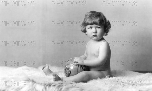 Naked child with ball, 1930s, A baby sits naked on a fur rug and holds a ball in his hands, Historical photo