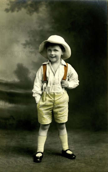 Boy with hat, 1920s, A little boy wears a straw hat and stands smiling in nature, Historical photo