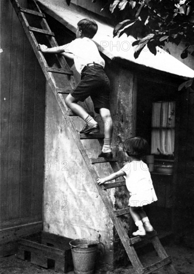 Two children on a ladder, 1920s, Two children climbing up a wooden ladder to a small building, Historical photo