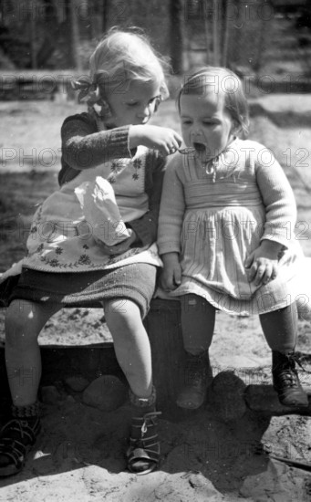 Girl feeding girl, 1930, Two little girls sharing a snack in a warm and friendly scene, Historical photo