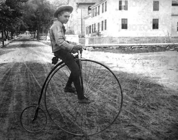 Boy on a penny-farthing, 1910s bicycle, Boy on an antique bicycle on a sandy street in a residential area, Historical photo
