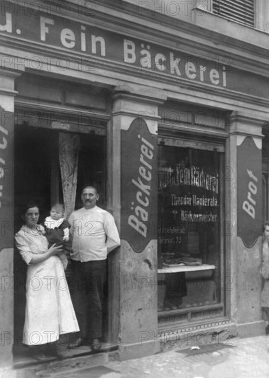 Couple in front of bakery, ca. 1915, Family posing in front of their traditional bakery with handwritten shop sign, historical photo