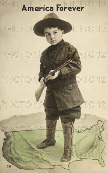 Little boy with uniform and rifle, America Forever, 1920s, Little boy in uniform with rifle standing on a USA map, text 'America Forever', historical photo