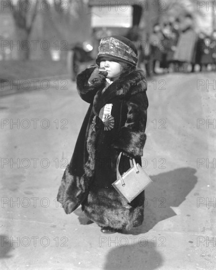 Child in too big fur coat smoking a cigarette, 1920s, Child in thick fur coat with hat and handbag on a street, historical photo