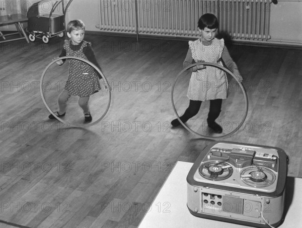 Two children playing with the Hulahup tyre, 1950s, Two girls dancing with tyres in front of a tape recorder on a wooden floor, Historical photo