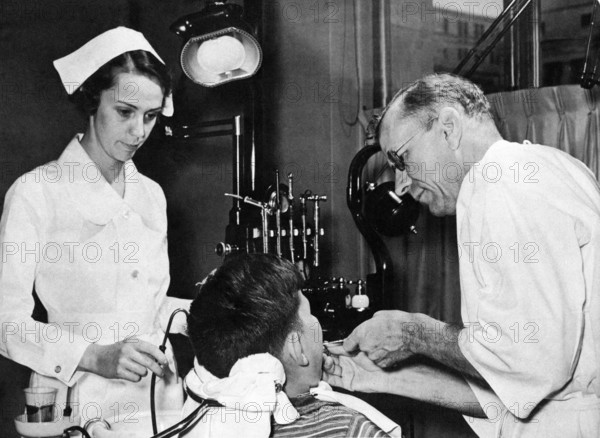 Dentist nurse child, 1930s, Dentist with nurse treating patients in a practice, historical photo