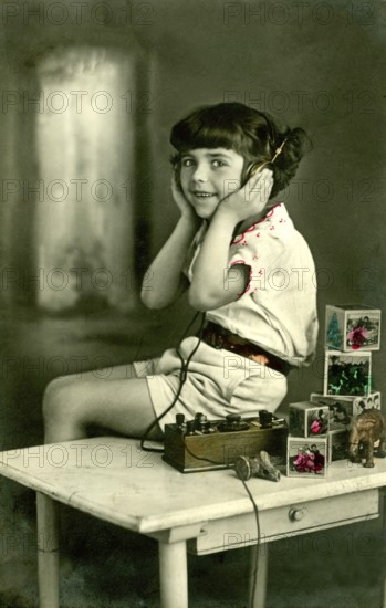 Child headphone radio, 1930s, girl with headphones sitting at a table with toys, historical photo