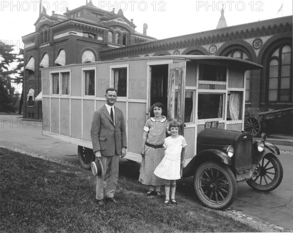 Caravan, 1930s, family in front of a historic car, possibly a mobile home, in front of an old building, historic photo