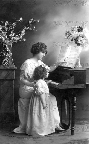 Woman and child with piano, 1920s, Mother and daughter sitting at the piano during music lessons, surrounded by flowers, historical photo