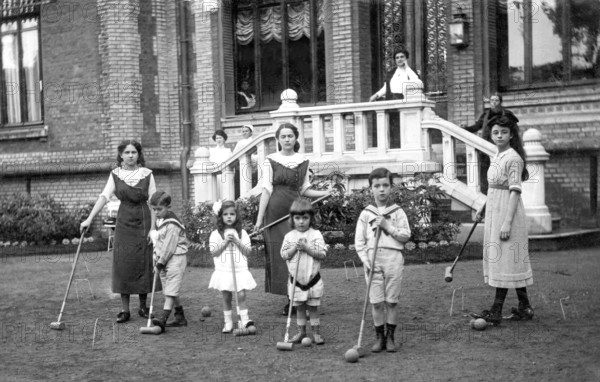 Family playing cricket, 1920s, group of children playing croquet in the garden in front of a large house, historical photo