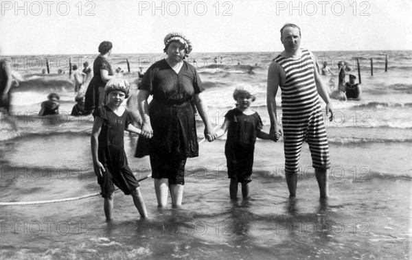 Family on the beach, 1920s, parents and children in the water, classic swimming costumes, relaxed atmosphere, historical photo
