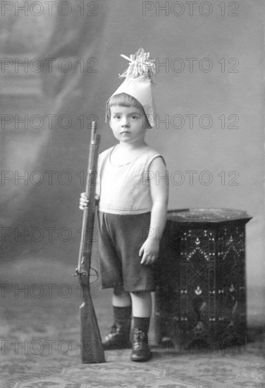 Little boy rifle, 1910s, boy in costume with toy rifle, serious face, vintage studio shot, historical photo
