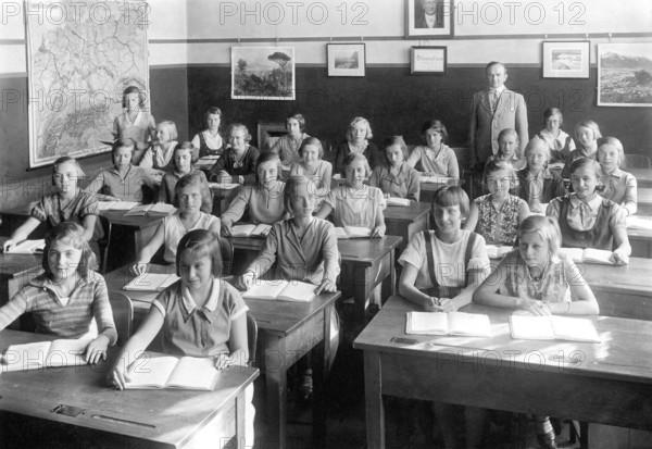 School class girls, 1930s, pupils and teacher in a classroom with maps on the walls, historical photo