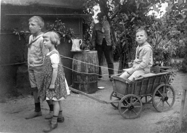 Children playing with carts, 1920s, children pulling a wooden cart in the garden, playful and communal atmosphere, historical photo