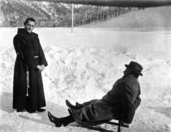Monk and man in the snow, 1920s, Monk pulling a man in winter clothes on a sledge through the snow, historical photo