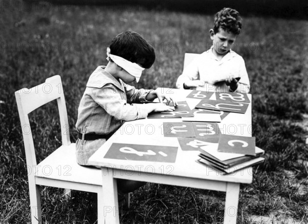 Blindfolded eyes, 1920s, Two boys busy themselves with flashcards while one is blindfolded, historical photo