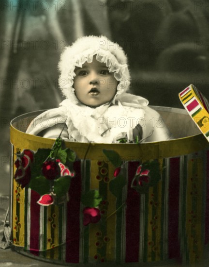 Baby in a gift box, 1930s, A toddler appears from a colourful box surrounded by flowers, Historical photo