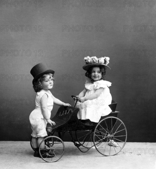 Two children with tricycle, 1920s, Two children in Victorian costumes playing on an antique tricycle, Historical photo