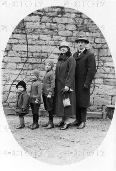 Family standing in a row, 1930s, Family in winter clothes standing together in front of a stone wall in black and white, Historical photo