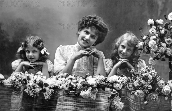 Woman with two girls, 1920s, Two girls and a woman smiling over a flower arrangement, Historical photo