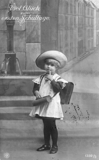 School enrolment, 1920s, A child poses with a school bag and hat in front of a painted city motif, Historical photo
