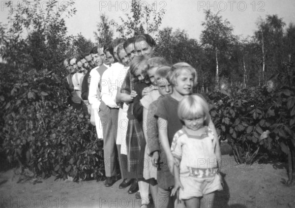 Standing in line, 1920s, family posing in a row in the garden, surrounded by plants, historical photo