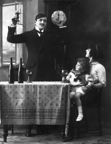New Year, man raising glass while woman with child sitting at table, old-fashioned photograph, historical photograph