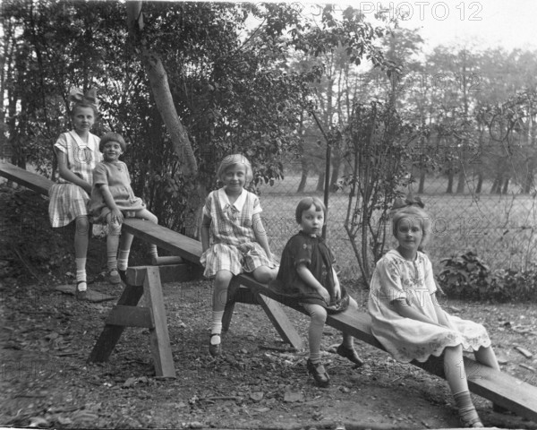 Five children on a seesaw, 1920s, Five children sitting on a swing outdoors, black and white photograph, Historical photograph