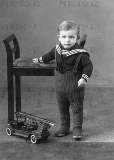 Little boy, toy, fire engine, 1920s, A toddler in a sailor suit stands next to a chair and a toy fire engine, Historical photo
